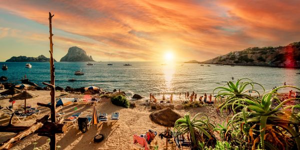 Picturesque view of Cala d'Hort tropical Beach, people hangout in beautiful beach with Es Vedra rock view during magnificent vibrant sunset glowing sun. Balearic Islands, Spain, Espana. Ibiza